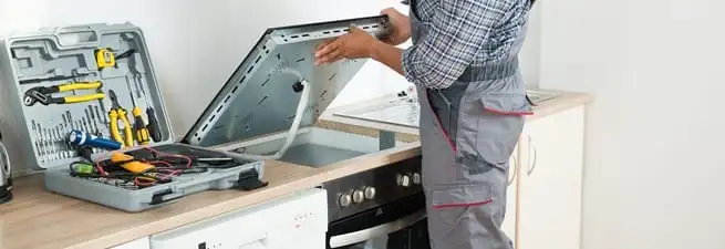 Cooktop repair technician lifting a built-in stovetop for service in Denver, CO