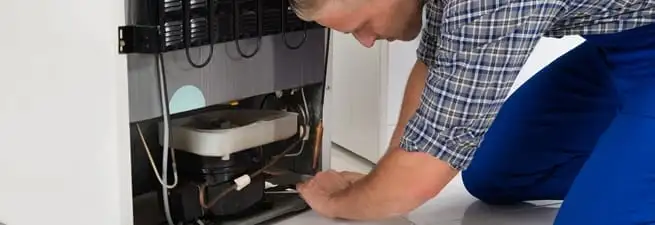 Refrigerator repair technician servicing the compressor and condenser area in Denver, CO