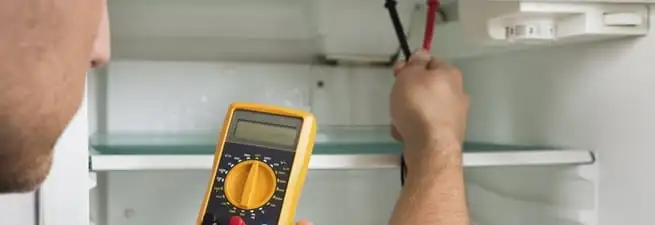 Refrigerator repair technician testing electrical components with a multimeter in Denver, CO