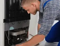 Refrigerator repair technician servicing the compressor and condenser area in Denver, CO